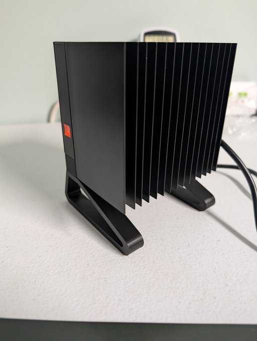 A black external SSD or hard drive with a finned heat sink design and angular stand, sitting on a white desk surface with a cable attached.