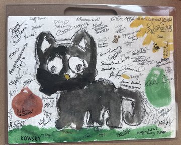Hand-painted artwork on a white surface featuring a black cat surrounded by handwritten notes, a sun, an apple, and signatures including 'KOWSKI' and a date that appears to be '1992'.