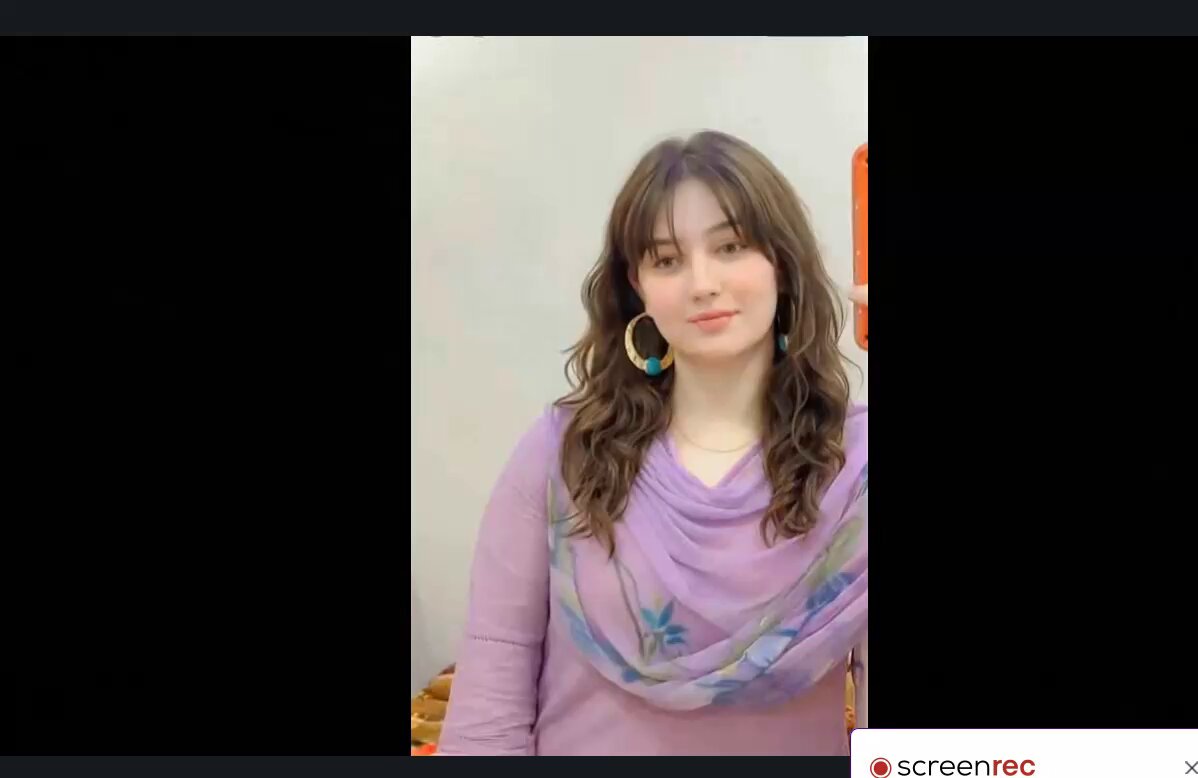 The image features a woman with long brown hair wearing a purple dress and earrings. She has her face turned towards the camera, giving off a friendly vibe. The background of the image is black, which contrasts nicely with the woman's attire. There are also some text elements in the image that read "Berlin, we're coming. On June 13th Superteam Germany is hosting the biggest Solana event Germany has ever seen and you'r invited". This suggests that the photo might be related to an upcoming event or gathering involving cryptocurrencies and blockchain technology.