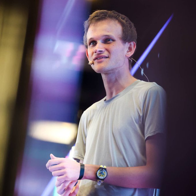 Vitalik Buterin, the co-founder of Ethereum, is shown on stage wearing a light gray t-shirt and a headset microphone, giving a presentation.
