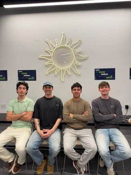 Four young men pose together in front of a decorative sunburst wall feature, appearing in high spirits after winning the Aleph Hackathon with their weekend project.
