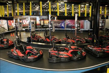 An indoor go-kart track featuring several red and black go-karts parked on the track, viewed through a protective barrier.