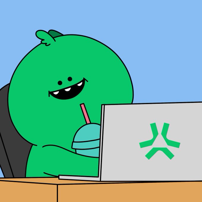 A cartoon green dinosaur-like character happily drinks from a cup with a pink straw while using a laptop that displays a green angry-face logo.