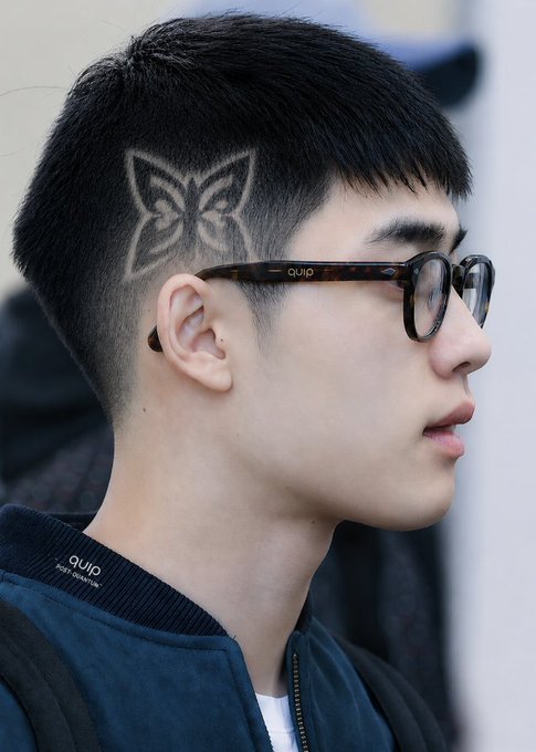 The image features a young man with short hair, wearing glasses and a blue jacket. He has a butterfly design shaved into his hair using a stencil. The photo also includes text that reads "Hanoi 41 C It's so hot that I decided to go get a haircut and requested a Quantum Echoes style with the Quip network logo @quipnetwork builds a post-quantum security layer to protect Bitcoin and crypto assets without needing a fork or wallet migration".