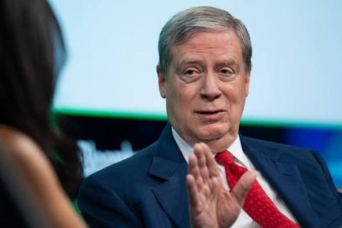 The image shows a suited older man speaking and gesturing during an interview. It accompanies a post about U.S. money printing, dollar debasement, and potential collapse of the fiat monetary system.