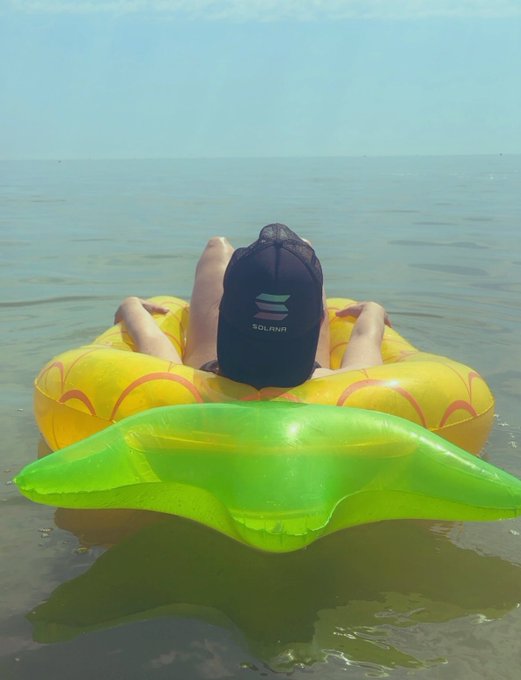 A person wearing a black hat is lying on an inflatable yellow pineapple float, enjoying their time in the water.