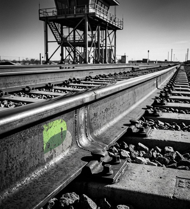 A black-and-white photograph of railroad tracks with a watchtower in the background, accented by a bright green Ethereum logo painted on the rail, symbolizes the "rails" being built for Ethereum's L2 tokenization boom mentioned in the post.