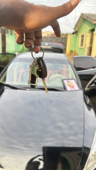 A hand holds up car keys triumphantly in front of a sleek black car, celebrating a milestone first purchase — likely a vehicle — symbolizing financial success achieved through Web3 ventures.