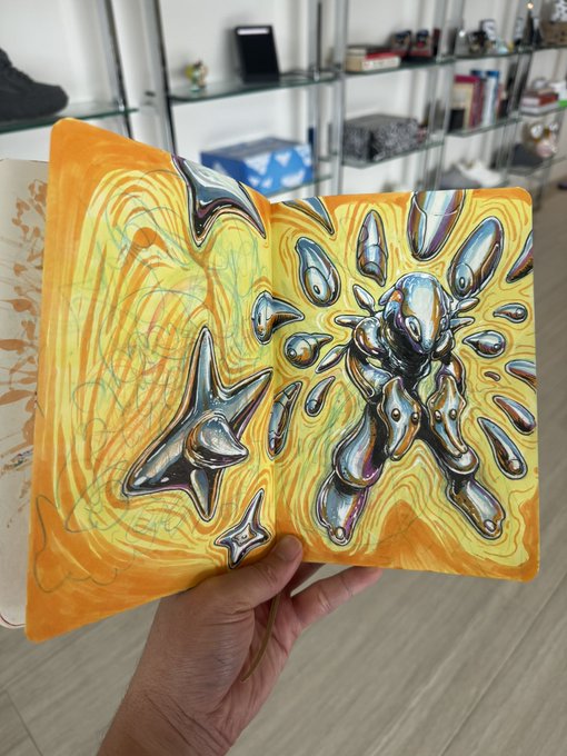 A hand holds open a sketchbook displaying an intricate surreal drawing of metallic, chrome-like organic shapes against a vibrant yellow and orange marbled background, created with Copic markers and Microns. The artwork showcases the artist's traditional medium preference and hints at the potential series of free community Mints they mentioned.