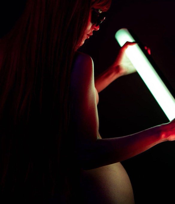 A profile shot of a woman in silhouette holding a glowing green light tube against a dark background. The bright green light visually represents the "green candles" mentioned in the post, a term used in trading to signify upward price movement.