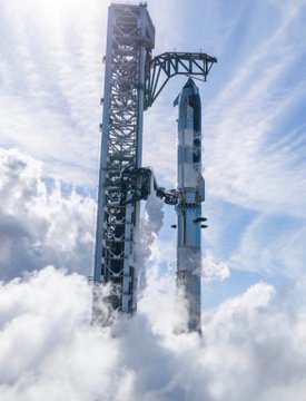 A SpaceX Starship rocket on its launch tower being captured by the chopstick arms amid thick clouds.