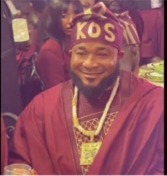 A low-resolution, meme-style image shows a smiling man wearing a red robe, gold chains, and a red headpiece with the text 'KOS'.