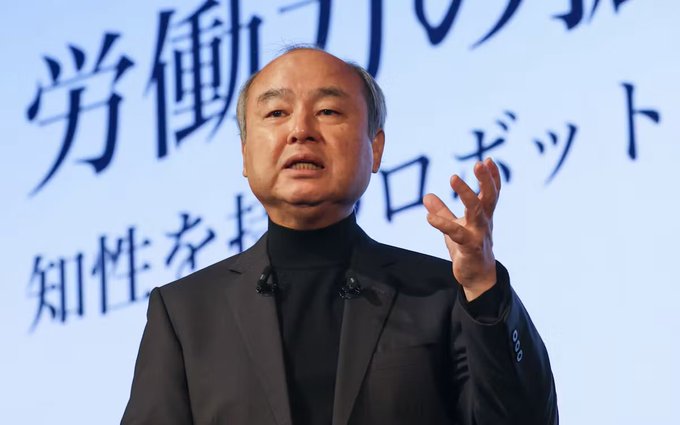 SoftBank Group CEO Masayoshi Son gestures while speaking, with Japanese text about labor and robotics visible in the background, in an image accompanying news of SoftBank's reported consideration of acquiring U.S. security giant Allied Universal.