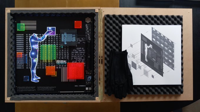 An open wooden display box with foam padding contains an artistic print of a blue glowing human figure interacting with computer components, alongside documentation materials and black gloves.