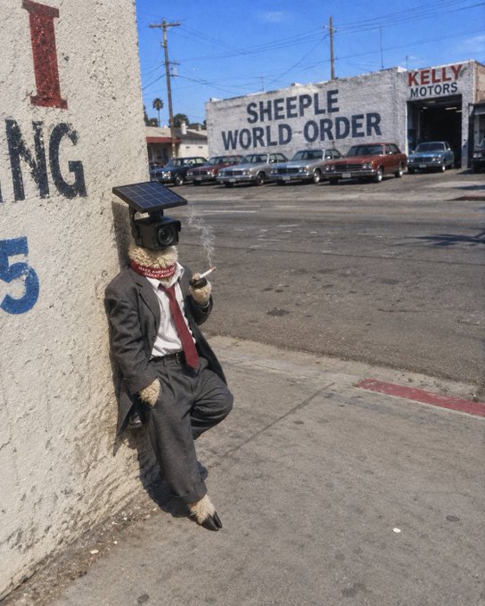 A person in a gray suit with a security camera and solar panel for a head, smoking a cigarette while leaning against a wall, with a 'SHEEPLE WORLD ORDER' billboard visible across the street.