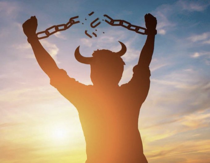A silhouetted figure with horns and raised arms breaks free from chains against a sunset sky.