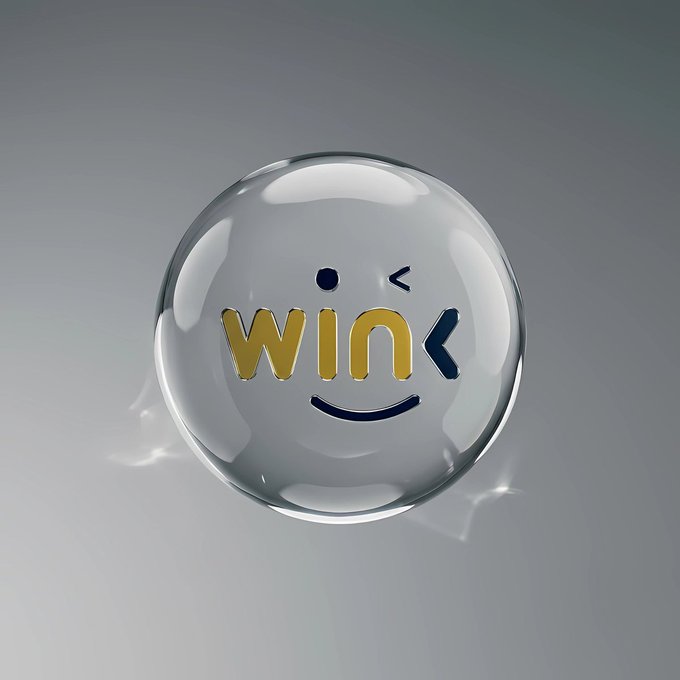 A transparent glass orb features a smiling face design with the text "wink" in yellow and dark blue letters, with one eye winking, set against a gray background.

The winking face visually reinforces the WINK brand name while symbolizing the playful "wink of randomness" referenced in the post's tagline "Where Randomness," connecting the dApp's identity to the idea of transparent, verifiable randomness in decentralized outcomes.