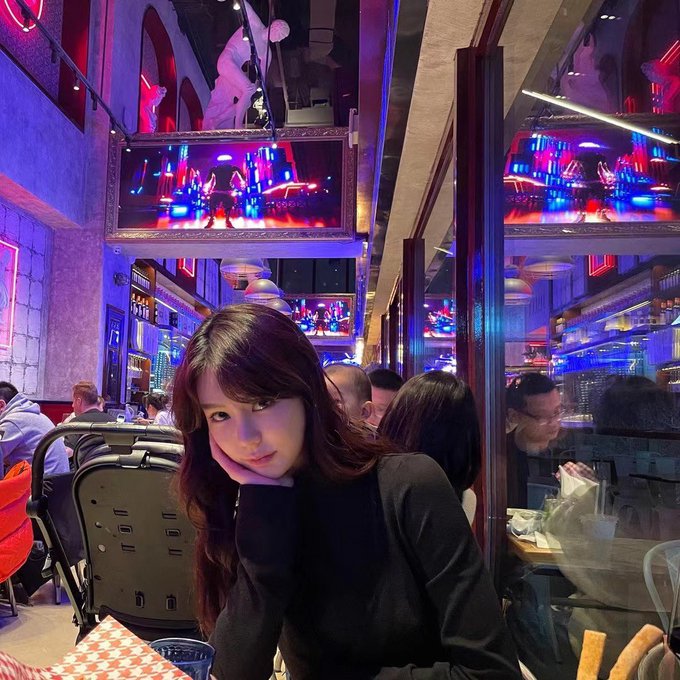 A young woman poses for a photo in a vibrant restaurant with neon lights and a bar area in the background.
