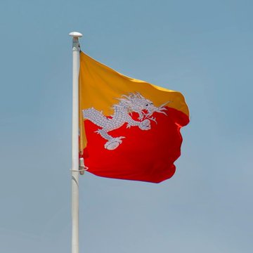 The flag of Bhutan, featuring its national symbol, the Druk, is shown waving against a blue sky. This image is relevant as Bhutan's Gelephu Mindfulness City has appointed 3iQ to manage part of its Bitcoin treasury.