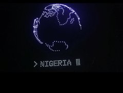 A dark screen displaying a pixelated, coiled dragon above the text '> NIGERIA' in a retro, computer-terminal style font.