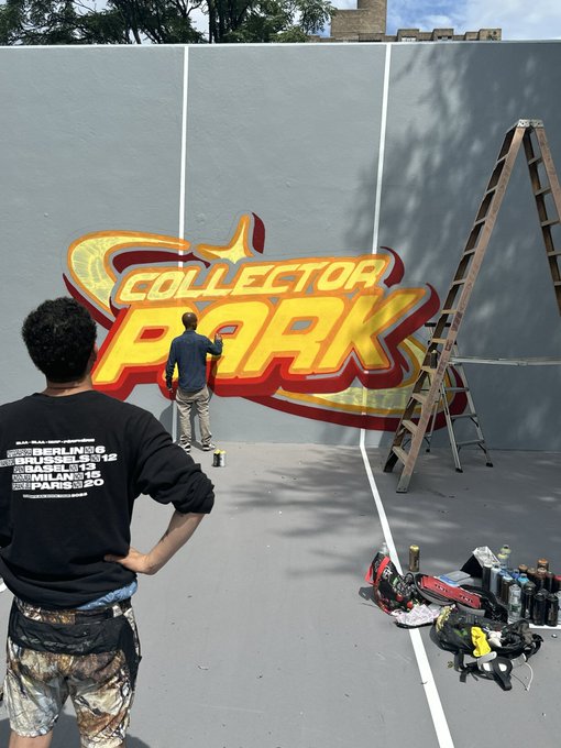 A scene showing an artist painting a 'Collector Park' mural in yellow and red lettering, while another person wearing a black sweatshirt listing cities like 'Berlin 16', 'Madrid 12', 'Basel 14', 'Milan 18', and 'Paris 20' watches, with spray paint cans and a ladder nearby.