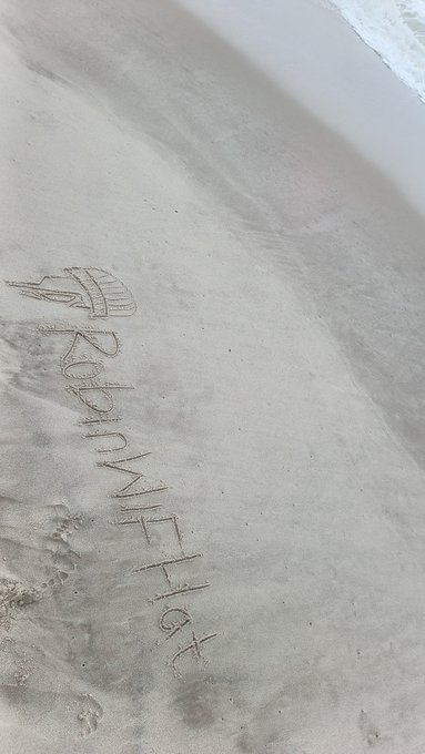 Aerial view of 'BEACHWITH-FR' written in large letters in the sand on a beach with the ocean visible in the upper right.