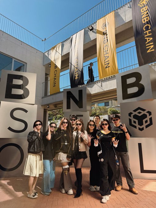 A group of people posing with hand gestures in front of large 'BSOL' letters and BNB Chain flags at an outdoor event.