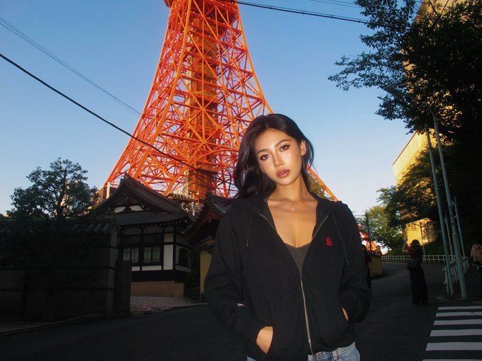 A woman in a black hoodie poses in front of Tokyo Tower, with the scene juxtaposed against a post recruiting long-term Solana-based "Backpack" token holders as volunteers. The striking backdrop contrasts the casual, urban portrait with the cryptocurrency community's call for dedicated participants.