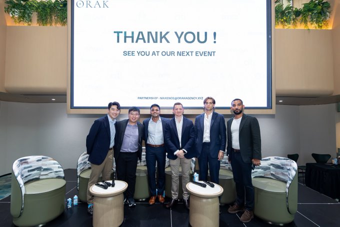 A group of six men in business attire posing together at an event with a screen behind them displaying 'THANK YOU! SEE YOU AT OUR NEXT EVENT' with partnership info 'IMEXNC@ORAKAGENCY.XYZ'.