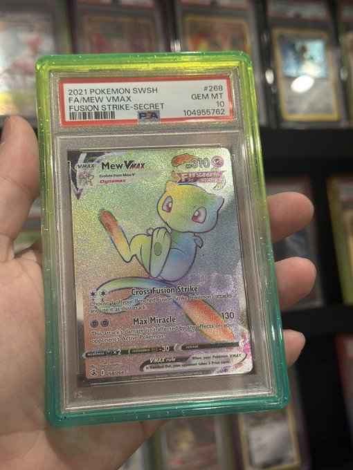 A hand holding a PSA 10 Gem Mint graded 2021 Pokémon SWSH Fusion Strike Mew VMAX holographic card (#288), certified with serial number 104955762, displayed against a background of other graded cards.