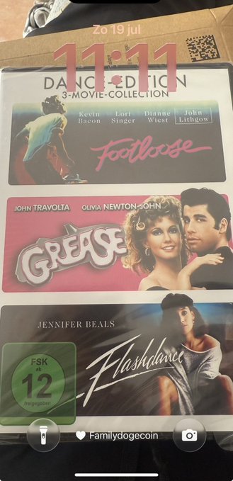A 11:11 timestamp on a phone photo of a 3-Movie Collection DVD set featuring Footloose, Grease, and Flashdance, posted by Familydogecoin.