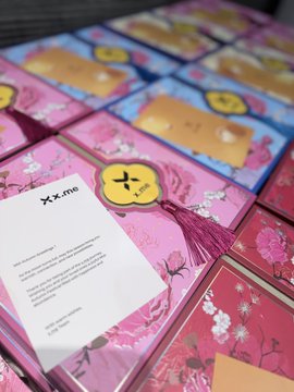 A close-up photo of several decorative pink boxes with floral designs and gold tags, one tagged "XZ+me", with a printed information card resting on top.