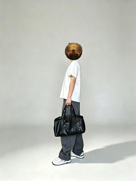 A person in a white t-shirt and gray pants holding a black duffel bag, standing in profile against a light gray background, with their head replaced by an image of a sesame seed bun.