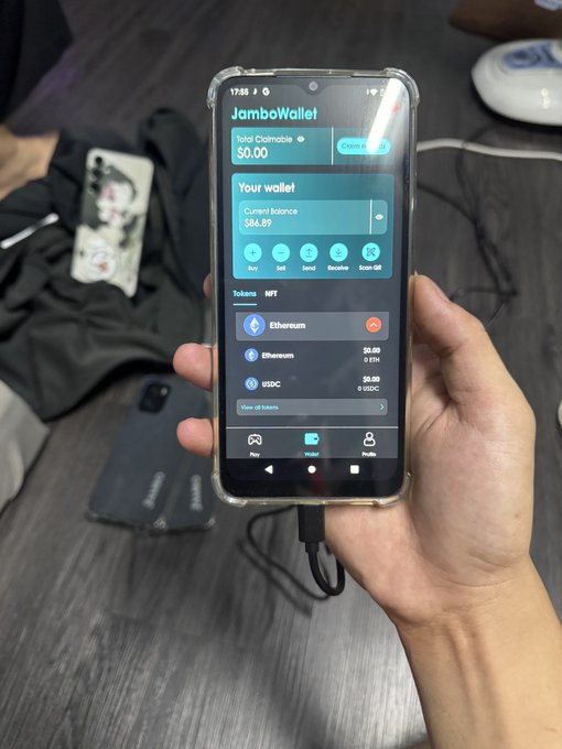 A hand holding a smartphone displaying the 'JamboWallet' app with a current balance of $66.67, showing options for Buy, Sell, Send, Receive, Scan QR, and a Tokens list including Ethereum and USDC.