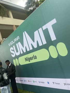A large green banner reads '#SOLANA SUMMIT Nigeria' with sponsor logos along the bottom, while a person in a black suit stands in front of it looking down.