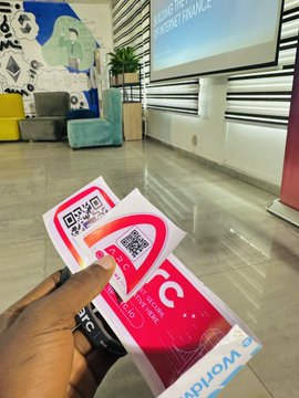 A first-person photo of a hand holding red and white promotional cards with QR codes in what appears to be an office or lobby setting.