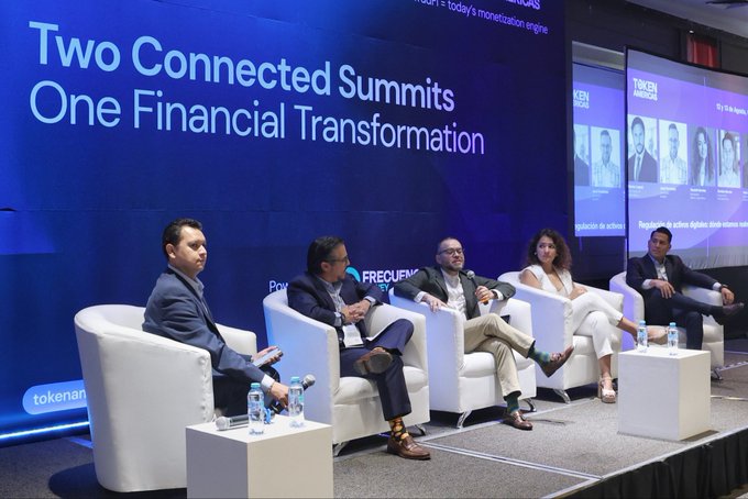 A panel of five people seated in white chairs on stage at a financial summit, with a large screen behind them reading 'Two Connected Summits One Financial Transformation'.
