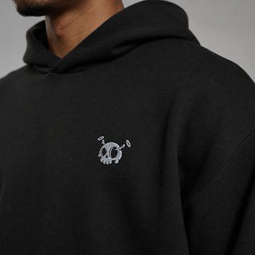 A close-up shot of a person wearing a black hoodie featuring a small embroidered skull and crossbones logo on the chest.