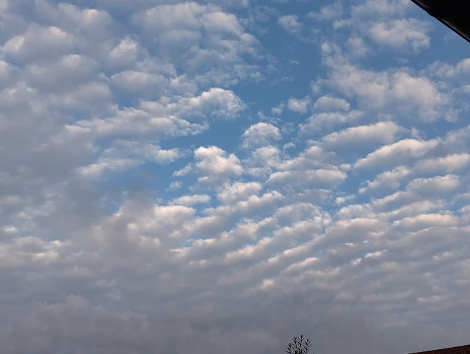 A daytime sky filled with scattered, patchy clouds in varying shades of white and gray against a blue background.