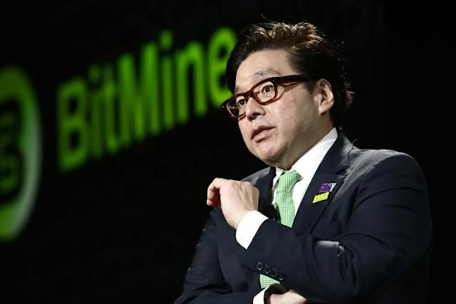 In this scene, a man dressed in a suit and glasses is standing next to a green "BITMINE" sign. The background appears to be a dark area with computer screens or some sort of digital display. In the text above him, there's a quote by a man named Tom Lee who talks about how Ethereum predictions could hit $250,000.