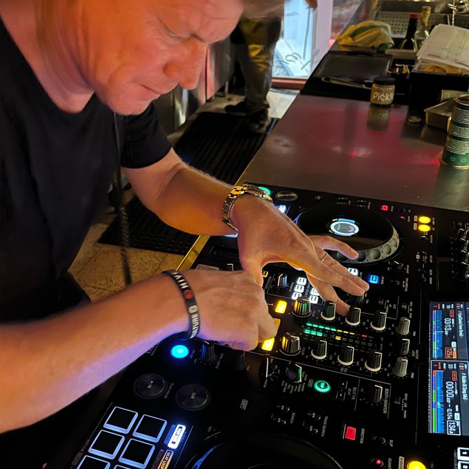 A DJ operating Pioneer DJ equipment at a bar or venue, with a can of PIRKKI beer visible on the counter beside the mixer.