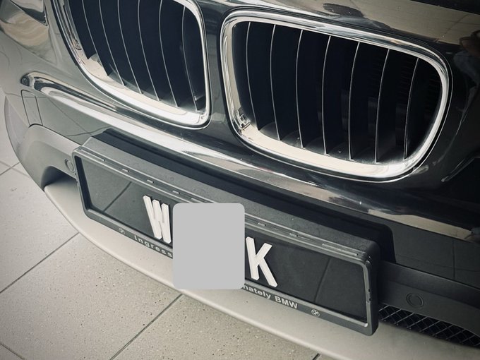 A close-up view of the front of a dark BMW shows the signature dual kidney grilles and a partially obscured license plate.