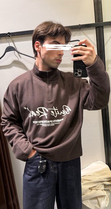 A young man takes a mirror selfie wearing a brown quarter-zip pullover with mirrored "Charlie Park" script lettering, paired with dark denim jeans. The casual retail try-on fits the "gmonad." vibe, showcasing a laid-back, stylish everyday outfit.