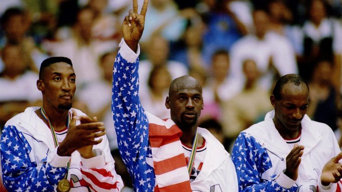 Basketball players in red, white, and blue USA uniforms celebrate on a podium, with one holding up two fingers in a victory pose.