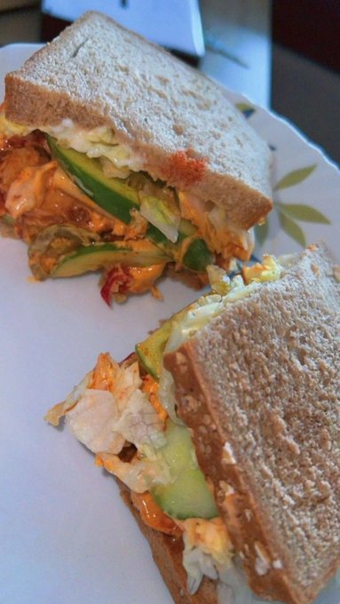 A cut sandwich on whole grain bread filled with chicken or fish, cucumber slices, and an orange sauce, served on a decorative plate.