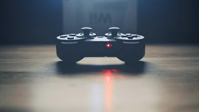 A black PlayStation-style controller sits on a wooden surface in dim lighting, with a glowing red LED casting a vivid reflection on the floor.

The image of the controller with its glowing red light visually symbolizes gaming culture, which relates to the post's commentary on market narratives and momentum—suggesting the playful, competitive nature of observing which trends "take hold" in this market cycle.
