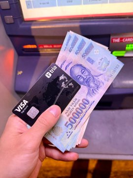 A hand holds a "tria" branded Visa Signature card and a stack of 500,000 Vietnamese Dong notes in front of an ATM. This image visually represents the traditional banking and cash system, contrasting with the "neobank space" and "PerpDEXs" mentioned in the accompanying post.