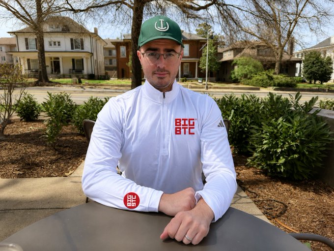 A man wearing a green cap and a white Adidas quarter-zip pullover with "BIG BTC" in red lettering sits at an outdoor table, with the post introducing him as Bitcoin CEO Rob Ham from the Titcoin Podcast, known for his association with Big Bitcoin.