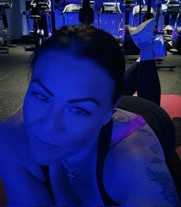 The image features a woman posing for a photo, wearing black pants and a pink top. She has tattoos on her arm and chest area. The caption of the image reads "NEVER UNDER-ESTIMATE A HEXICAN. I have all the fight necessary For GREATNESS V A L H A L L A Ya with me #HEXICAN". This message is related to the woman's body art, as it emphasizes that she embraces her tattoos and does not judge others based on their appearance or choices.