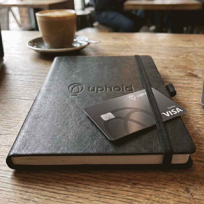 The image features a black notebook with a silver credit card, presumably an XRP (XRP) payment method, placed on top of a wooden table. The caption reads "Mornings hit different when you'r earning XRP". This suggests that the person using this notebook might be interested in cryptocurrency or digital payments and is likely to experience some differences in their morning routine due to the use of XRP as a payment method.